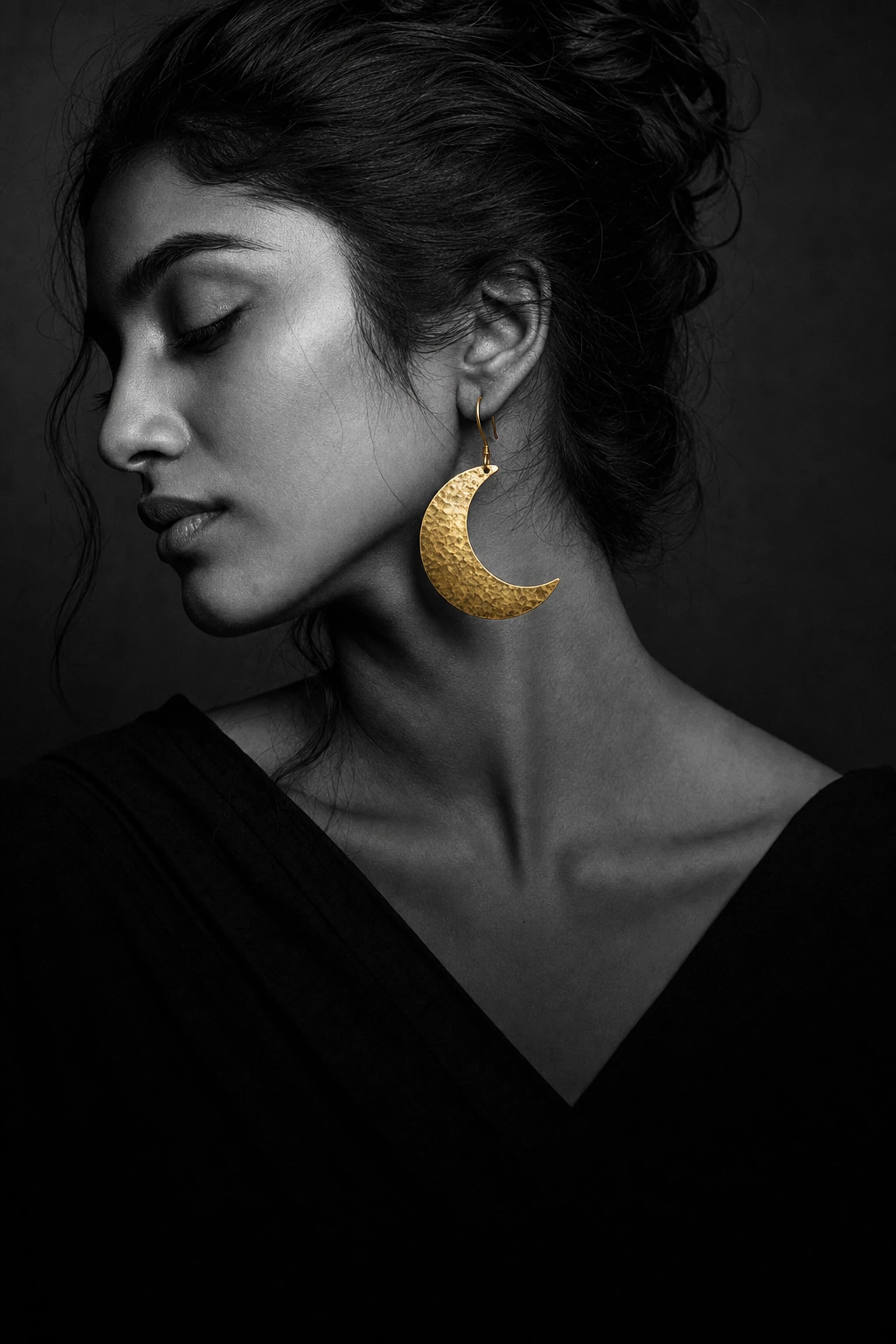 Black and white portrait of a woman wearing a large handmade hammered brass crescent moon earring — the brass is the only thing in colour